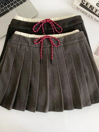 Gray pleated skirt with a pink drawstring on a white surface.