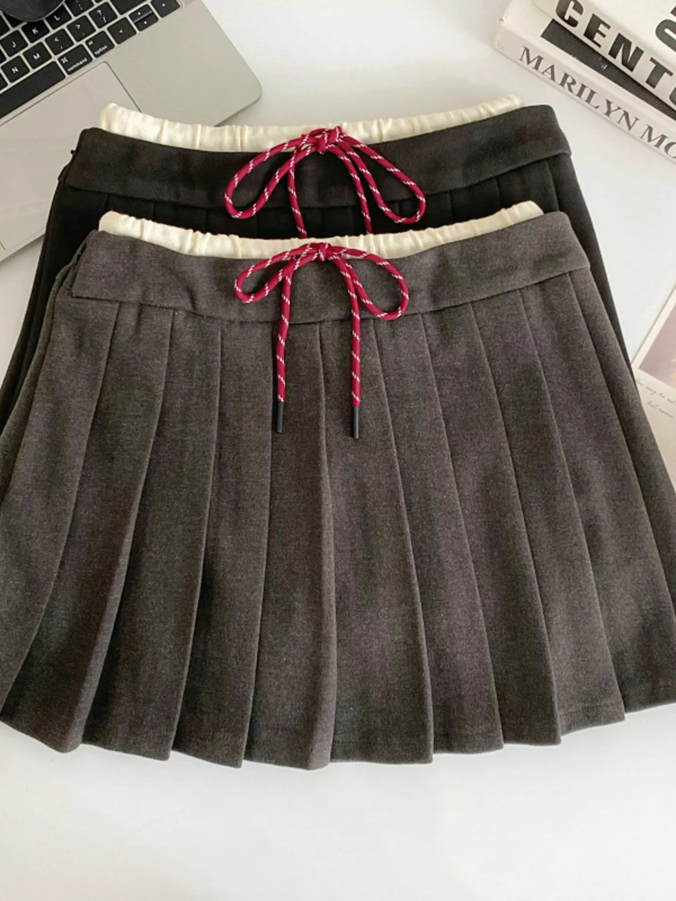 Gray pleated skirt with a pink drawstring on a white surface.