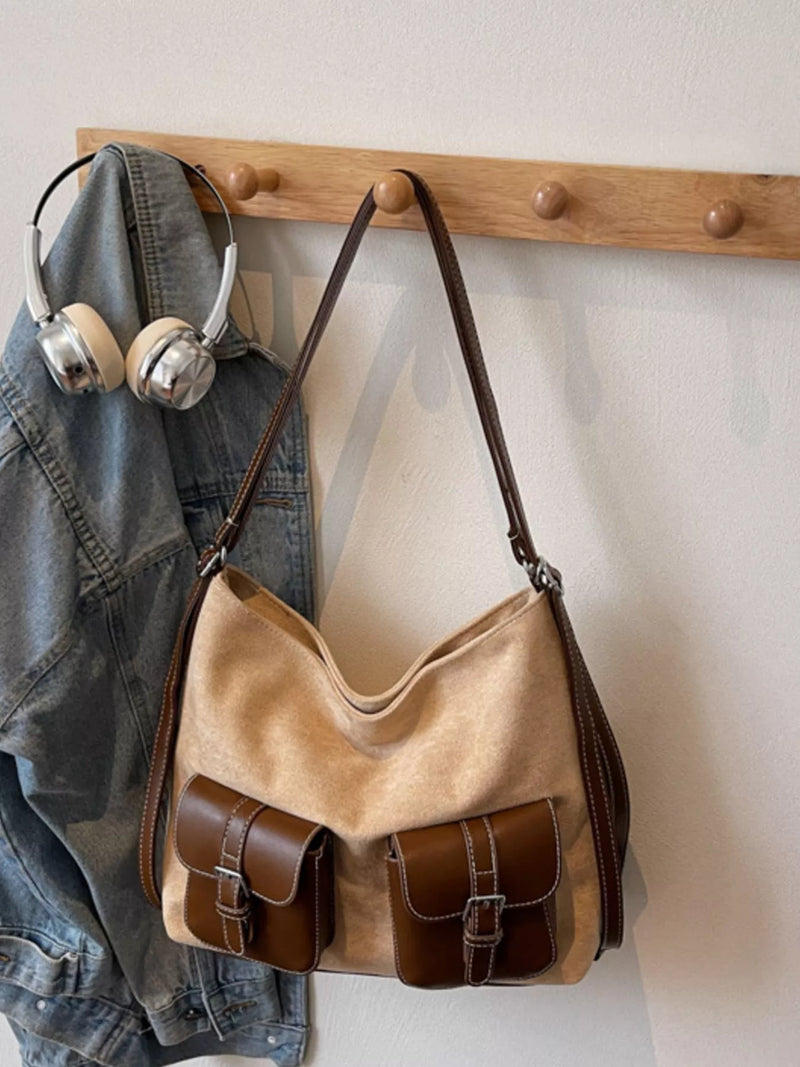 Brown leather handbag hanging on a wooden hook with denim jacket and headphones.
