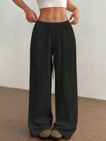 Person wearing black wide-leg pants with a white top against a plain background