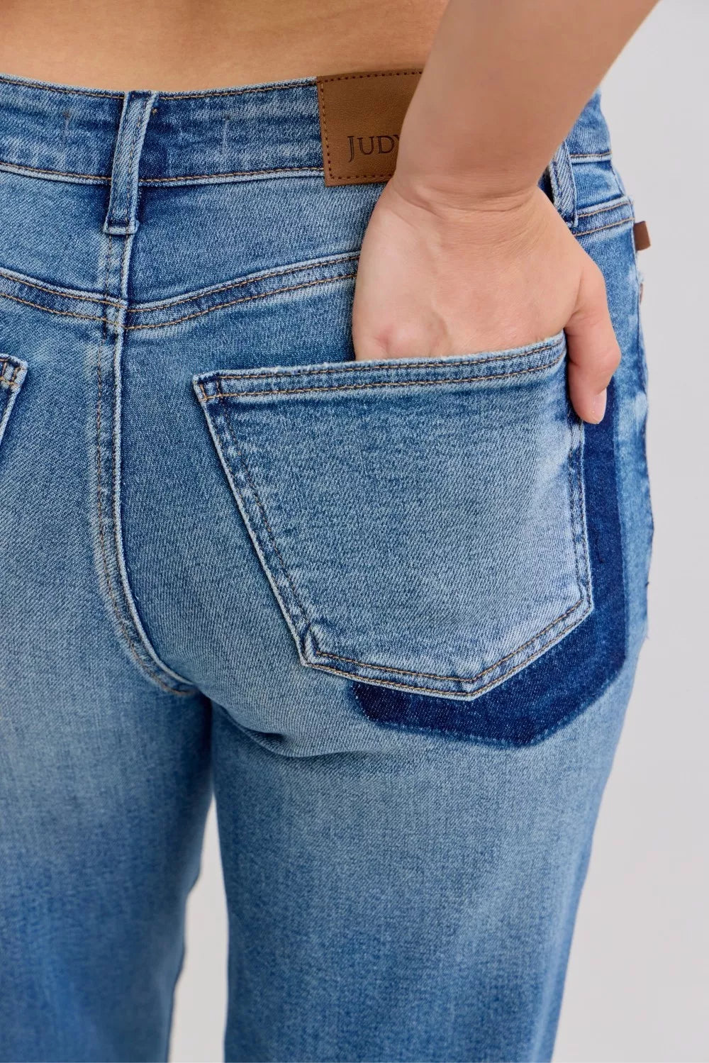 Close-up of blue jeans with a hand in the pocket on a light gray background