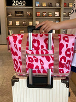 Person holding a pink leopard print bag over a white suitcase in a store setting.