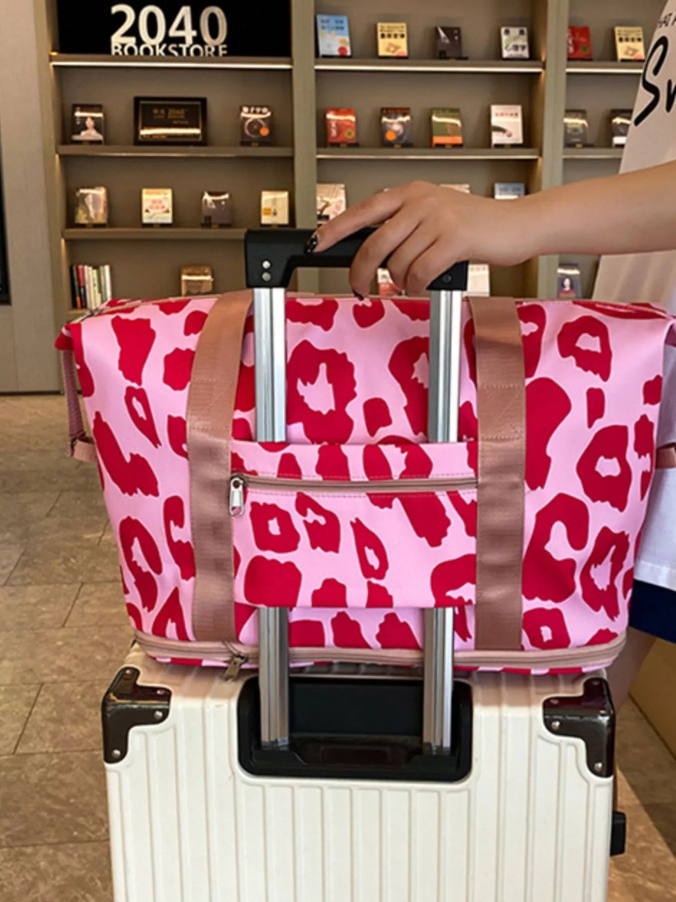 Person holding a pink leopard print bag over a white suitcase in a store setting.