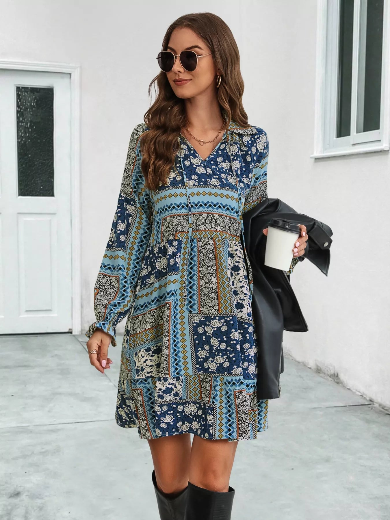 Woman wearing a patterned dress holding a coffee cup outdoors.