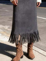 Person wearing a long dark gray suede skirt with fringe and brown boots on a street.