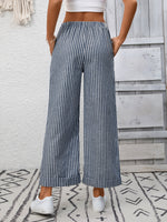 Person wearing blue and white striped wide-leg pants with a white top against a light wooden panel background.