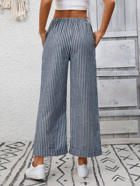 Person wearing blue and white striped wide-leg pants with a white top against a light wooden panel background.