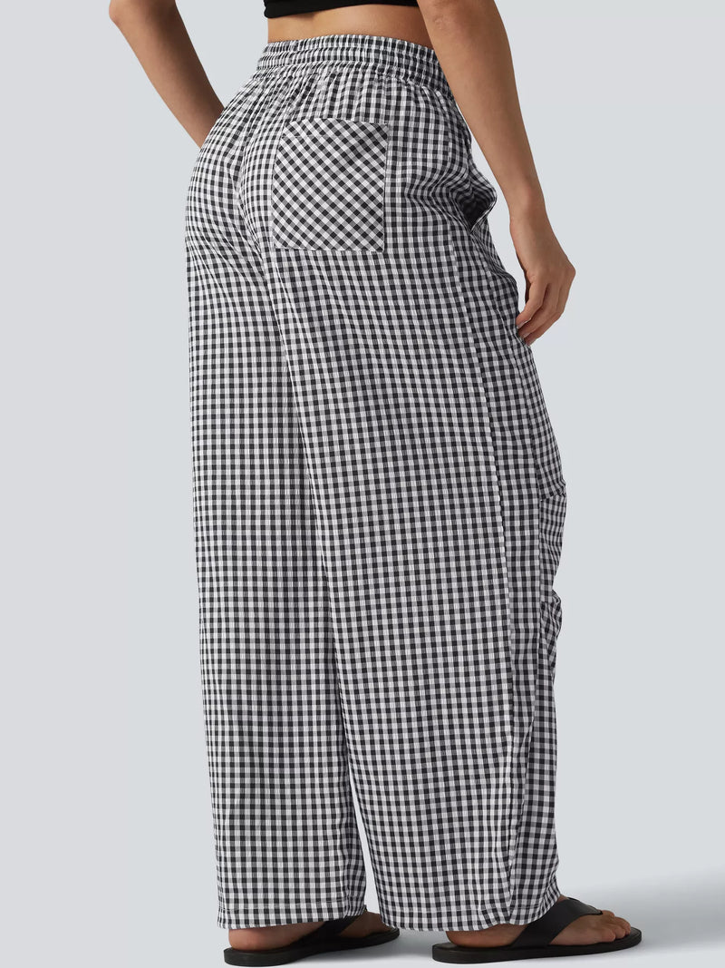 A person shown from the back wearing loose black-and-white gingham wide-leg pants with an elastic waistband and side pockets, paired with black sandals against a light gray studio background.