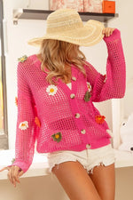 Person wearing a pink crochet cardigan with floral patterns indoors.