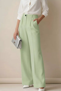 Person wearing light green pants and a white shirt, holding a silver clutch against a beige background