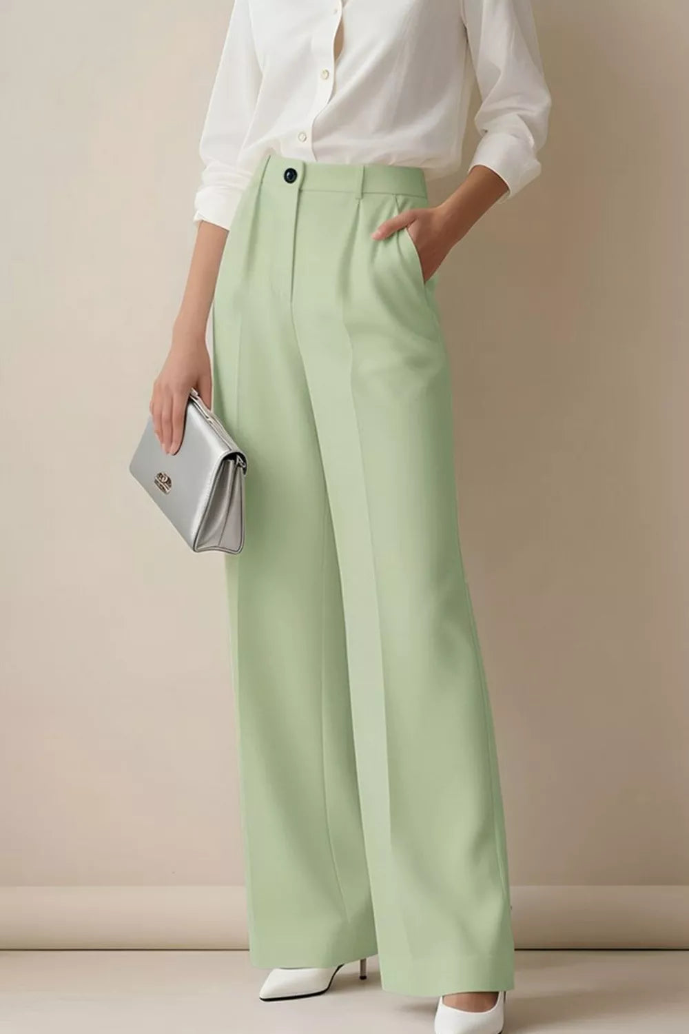 Person wearing light green pants and a white shirt, holding a silver clutch against a beige background