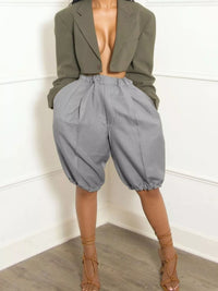Person wearing a green blazer and gray high-waisted pants against a white wall.