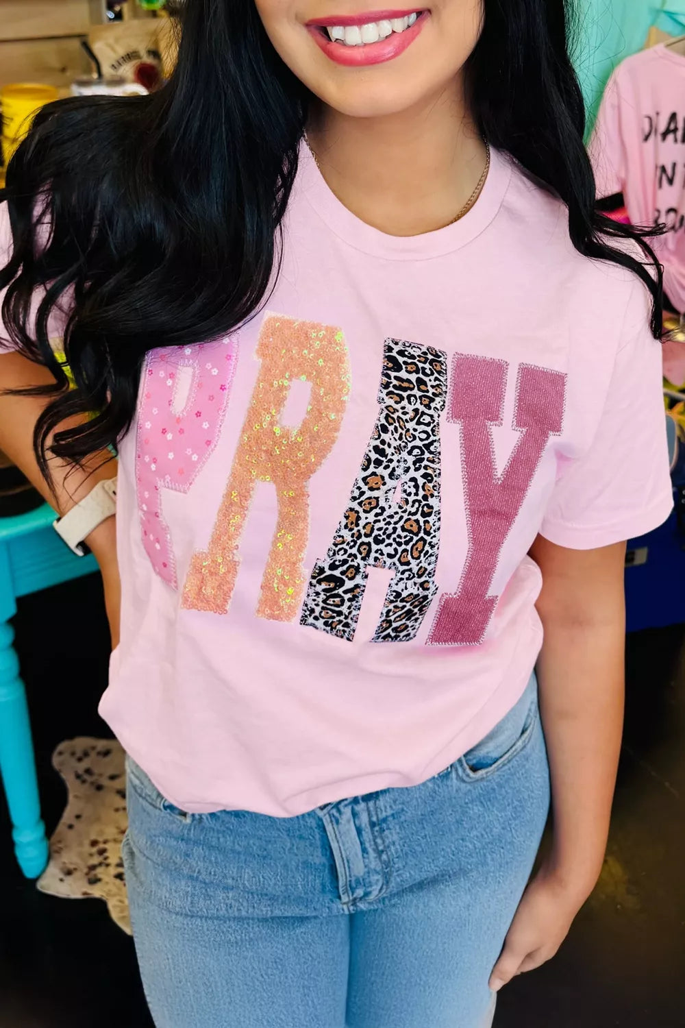 Person wearing a pink t-shirt with colorful text design in an indoor setting