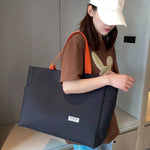 Woman holding a black tote bag with an orange strap indoors.