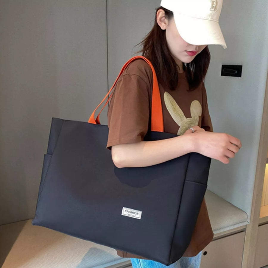 Woman holding a black tote bag with an orange strap indoors.