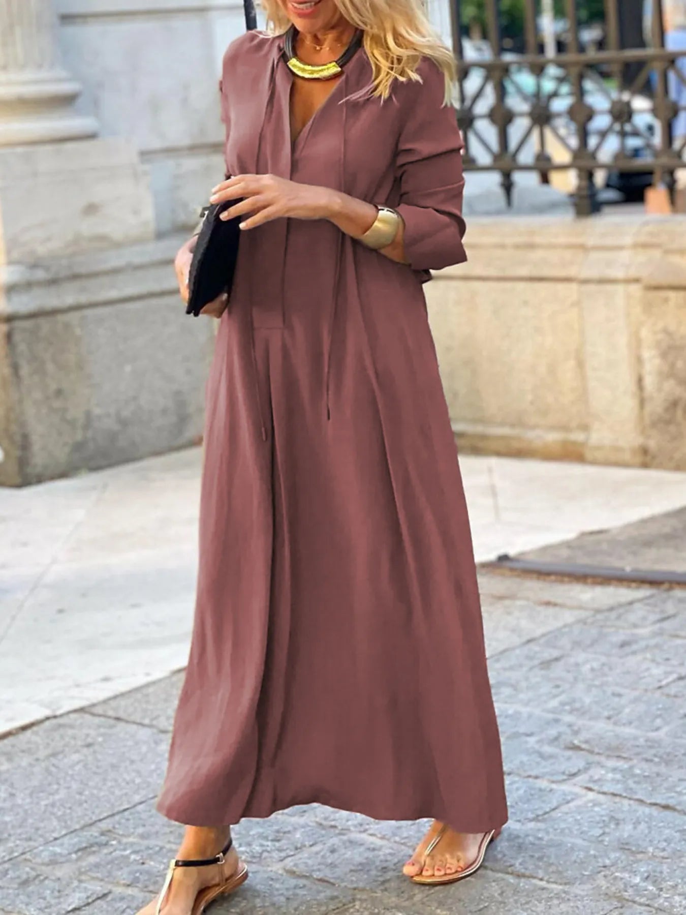 Woman wearing a long mauve dress standing on a stone pavement.