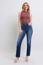 Woman wearing a sleeveless brown top and blue jeans on a light gray background