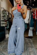 Person wearing a denim jumpsuit taking a mirror selfie in a clothing store.