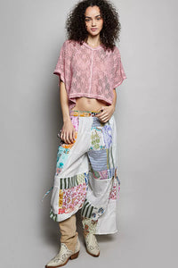Woman wearing a pink lace top and colorful patchwork skirt on a gray background
