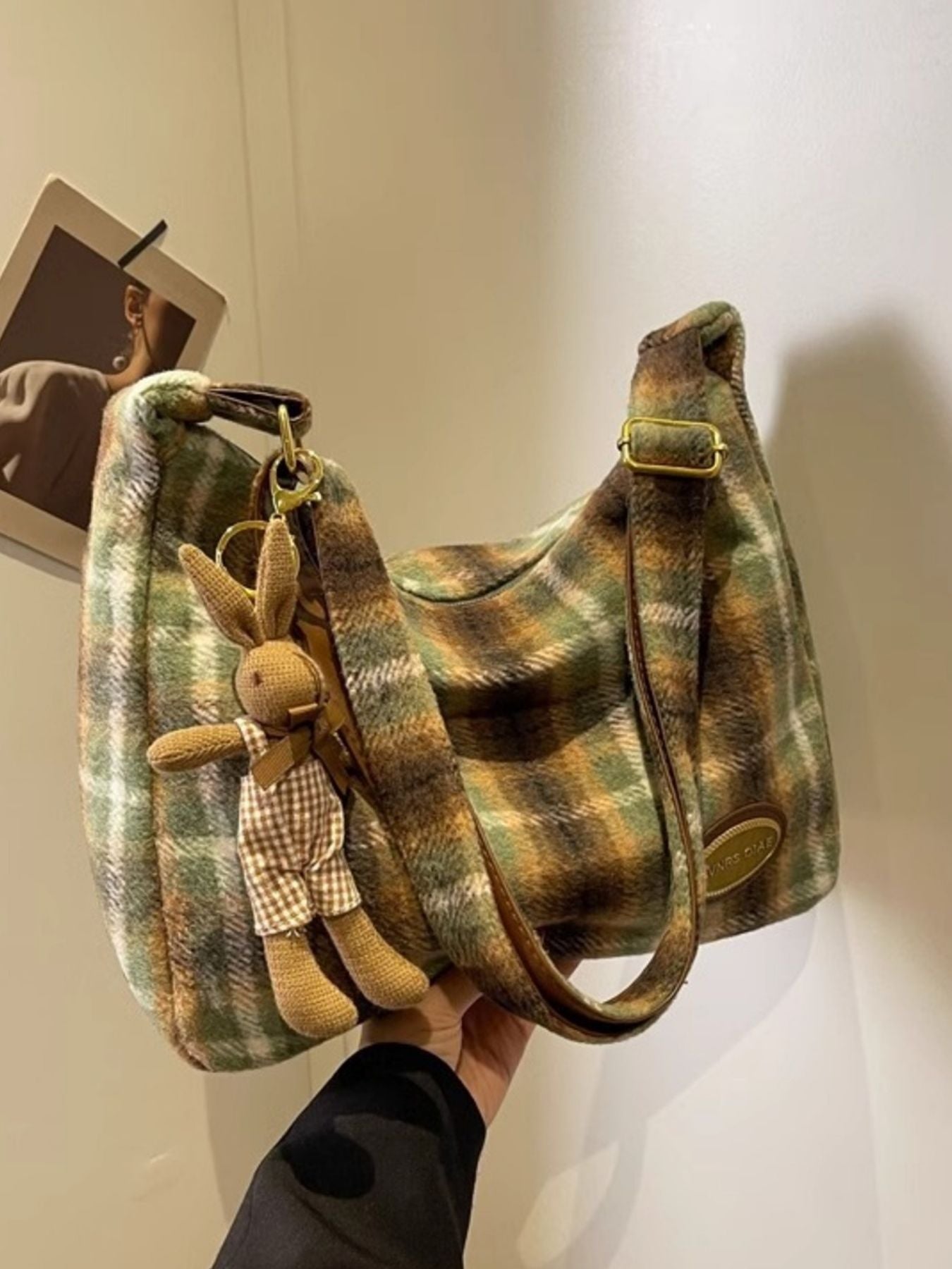 Plaid patterned handbag with a teddy bear keychain held against a neutral background