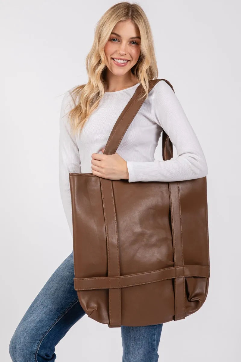 Woman holding a brown leather tote bag against a white background