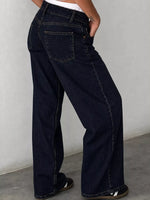 A person wearing dark navy wide-leg denim jeans, shown from the waist down, standing against a light gray wall.