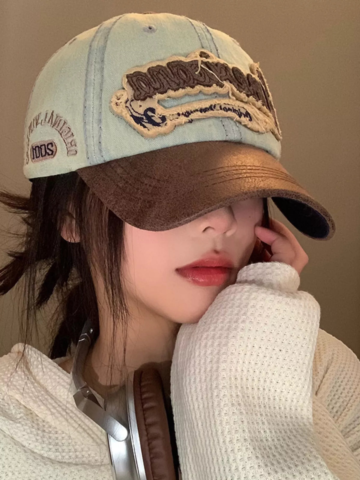 Person wearing a brown and beige cap with text, holding a phone to their ear.
