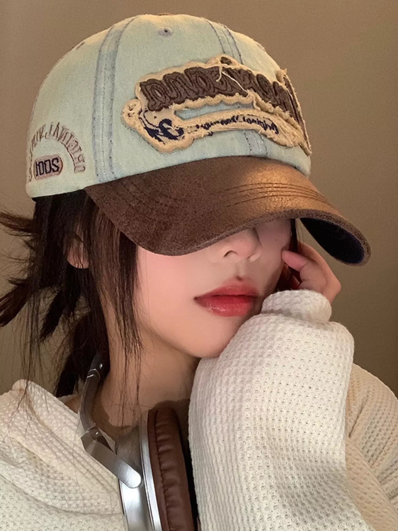 Person wearing a brown and beige cap with text, holding a phone to their ear.
