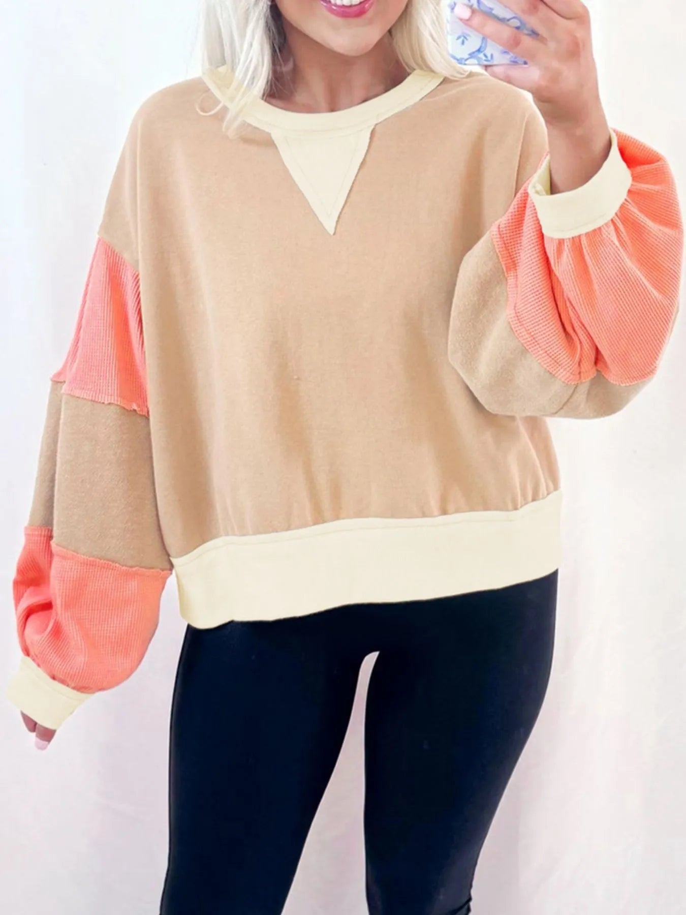 Person wearing a beige and coral sweater with black pants on a white background