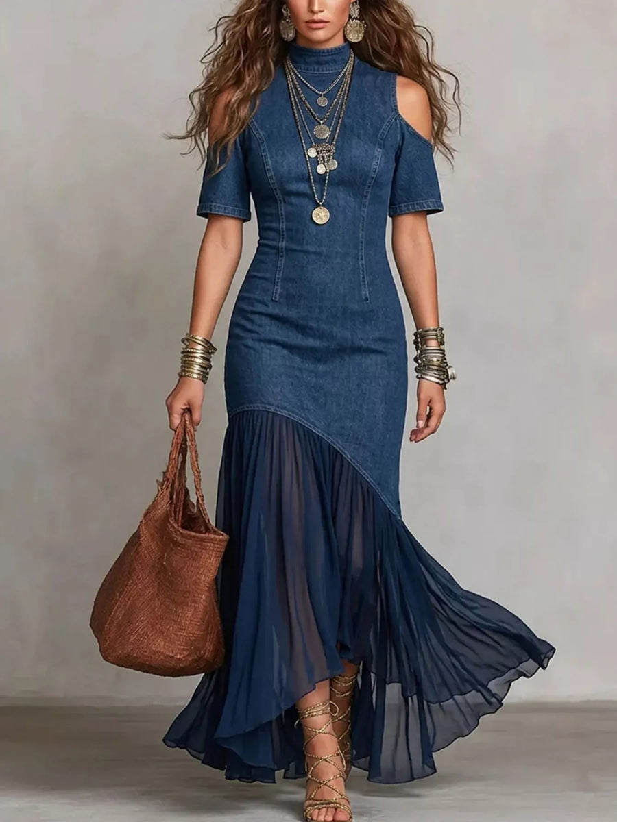 Woman wearing a blue dress with a brown handbag against a plain background