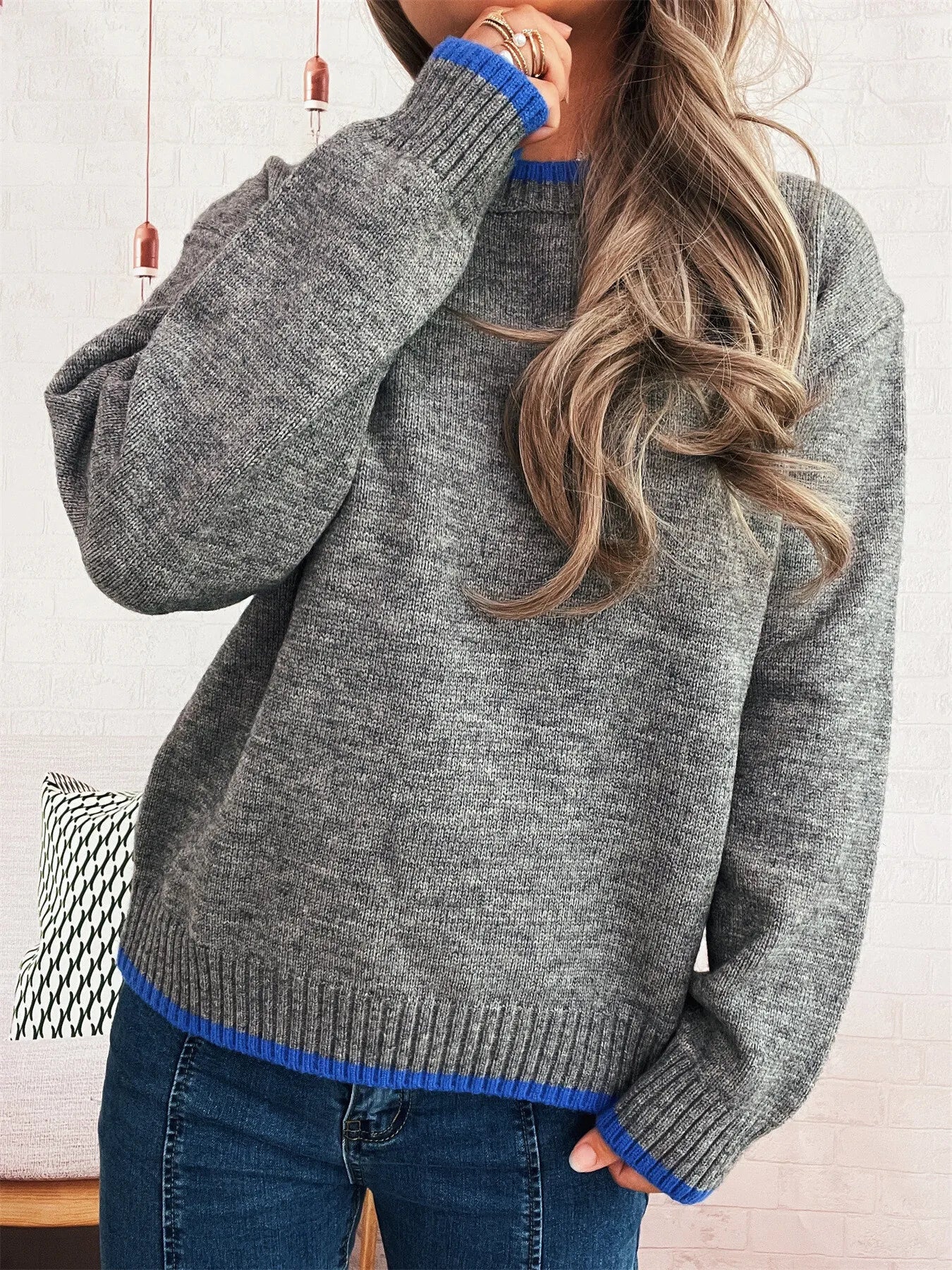 Person wearing a gray sweater with blue trim, sitting on a couch.
