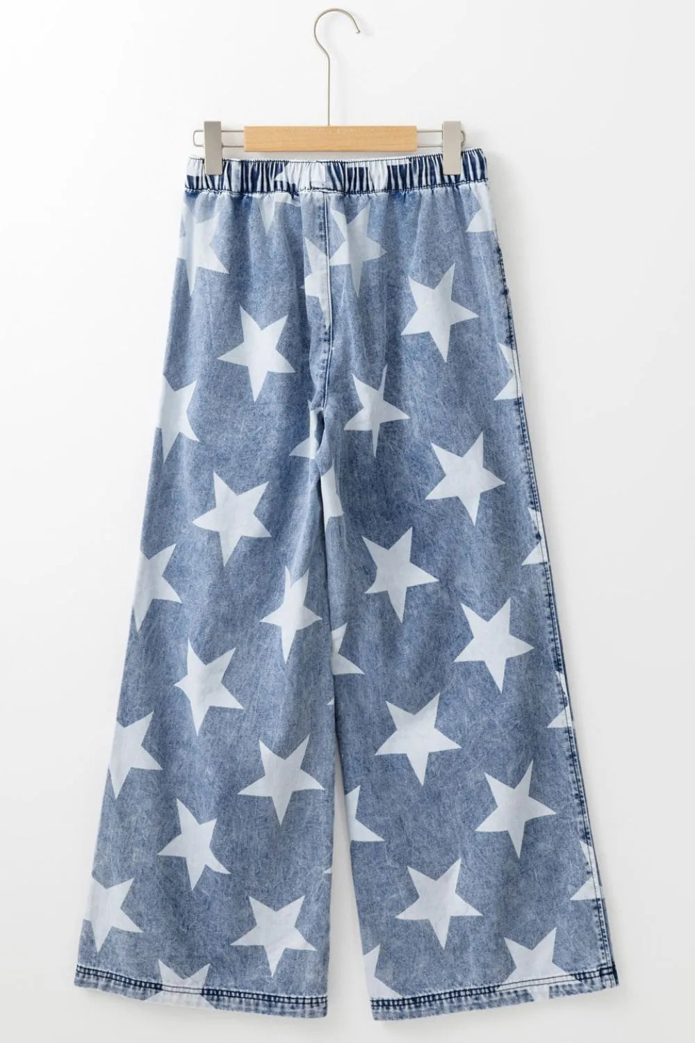 Blue denim pants with white star pattern on a hanger against a white background