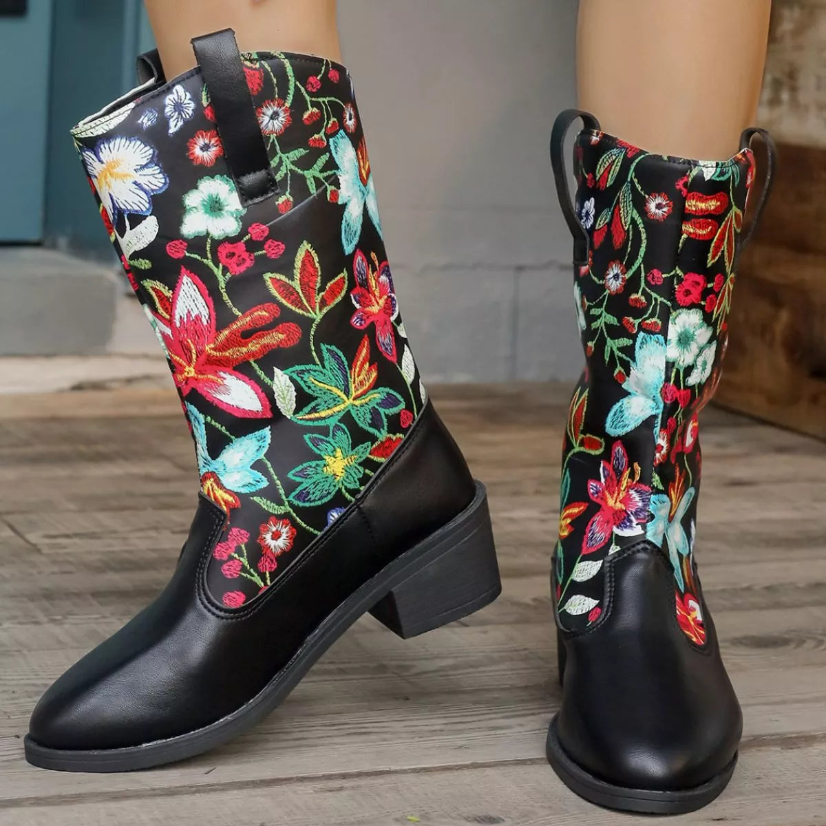 Black boots with colorful floral and butterfly patterns on a wooden floor.