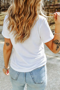 Person wearing a white t-shirt and light blue jeans with tattoos on arms outdoors.