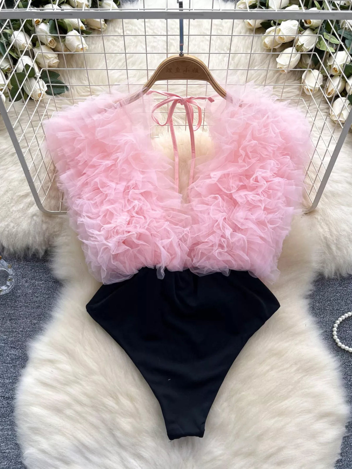 Pink fluffy top and black shorts on a hanger against a white floral background