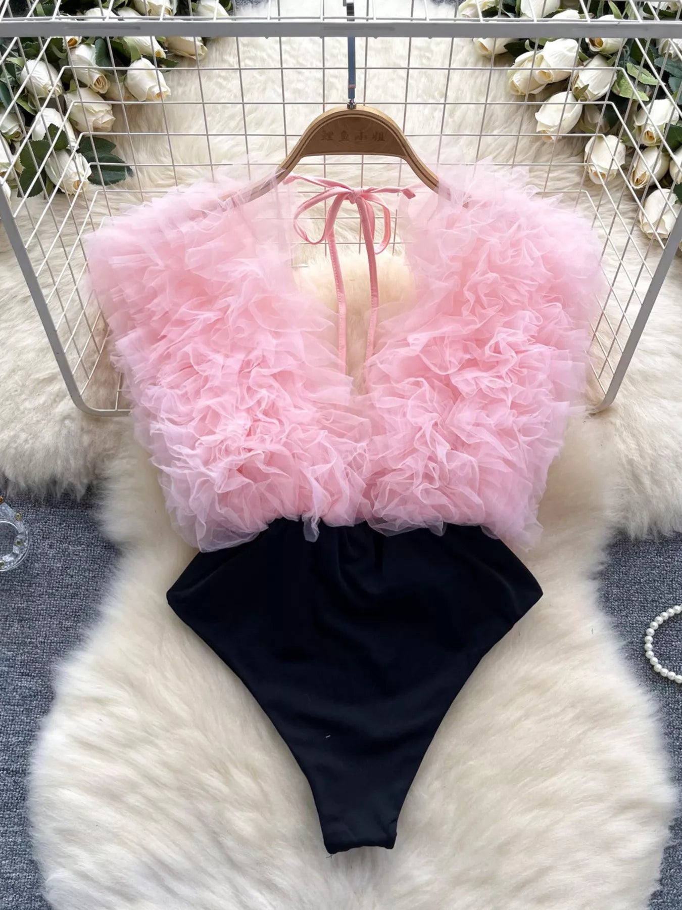 Pink fluffy top and black shorts on a hanger against a white floral background