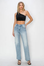 Woman wearing a black one-shoulder top and light blue jeans on a white background
