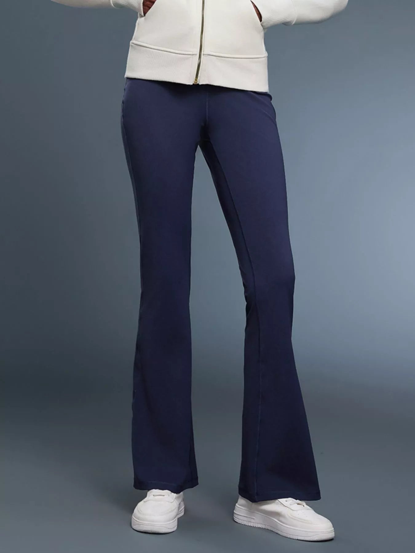 Person wearing navy flared pants and a white jacket on a gray background