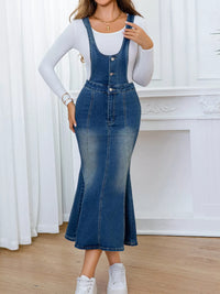 Person wearing a denim dress over a white long-sleeve shirt against a white curtain background