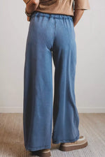 Person wearing blue wide-leg pants and a brown top against a neutral background