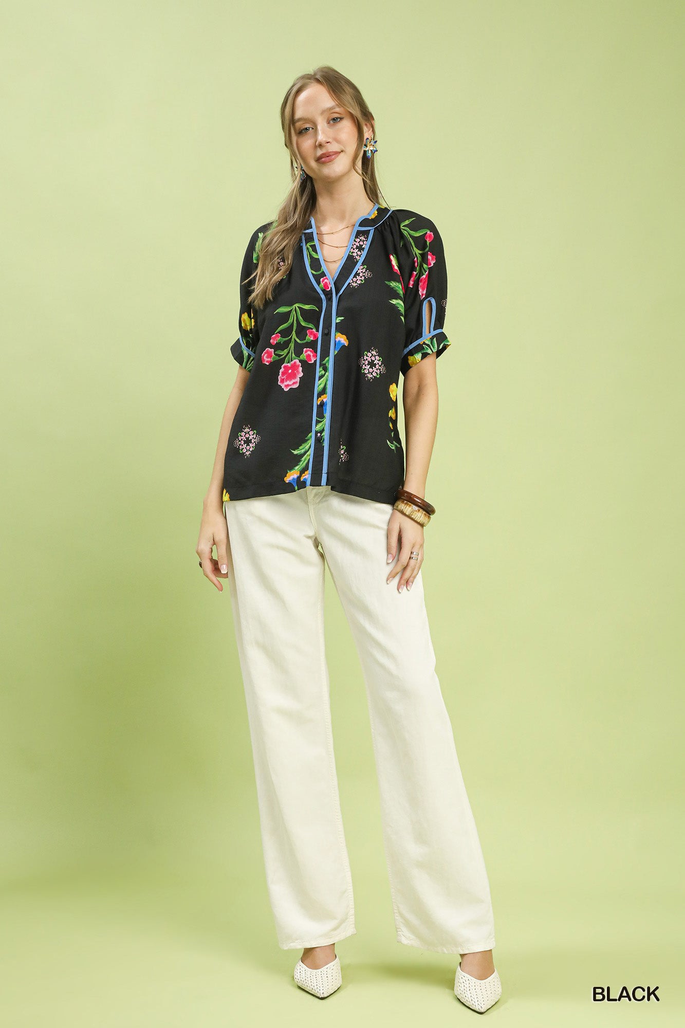 Woman wearing a black embroidered blouse and white pants on a light green background