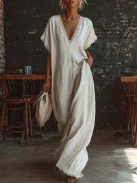 Woman in a white dress holding a beige hat in a rustic indoor setting.