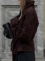 Person wearing a brown coat holding a black cup against a stone wall.