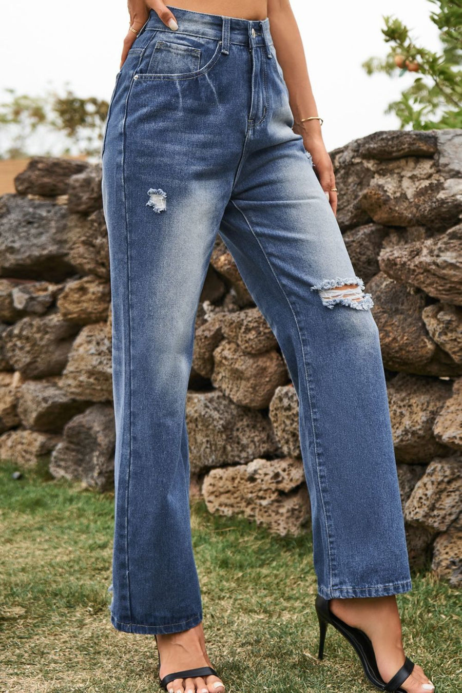 Person wearing blue jeans with a stone wall background
