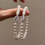 Pearl bracelets with purple gemstones held by a hand against a neutral background