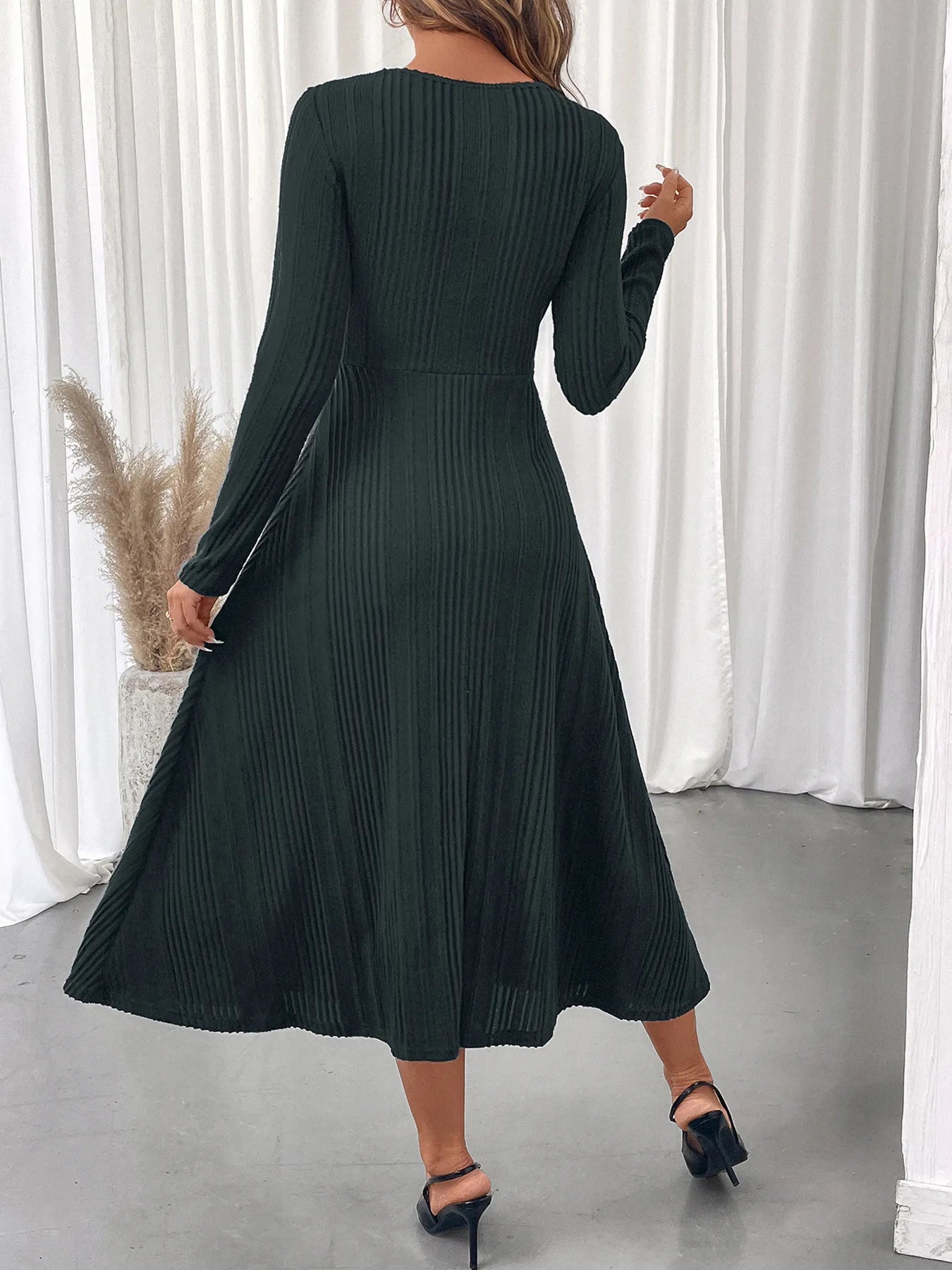 Woman wearing a dark green ribbed dress with long sleeves in a minimalistic setting.