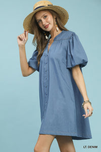 Woman wearing a blue denim dress and straw hat against a light blue background