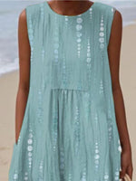 Person wearing a light blue dress with white patterns on a beach.