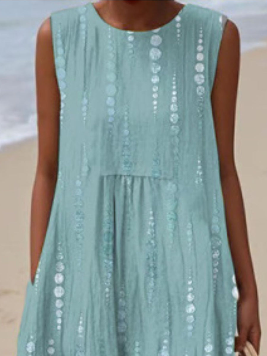 Person wearing a light blue dress with white patterns on a beach.