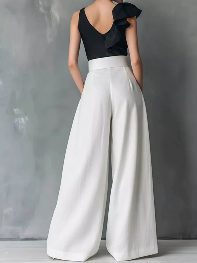 Person wearing a black top and white wide-leg pants against a gray background